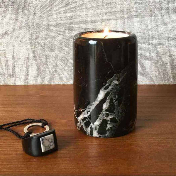 A black marble tea light candle holder sitting next to a black ring on a wooden shelf