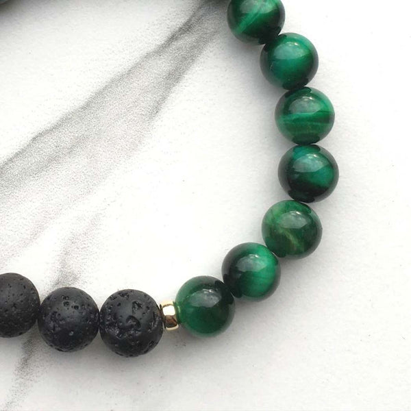 A green tigers eye and lava stone aromatherapy bracelet on a white marble background