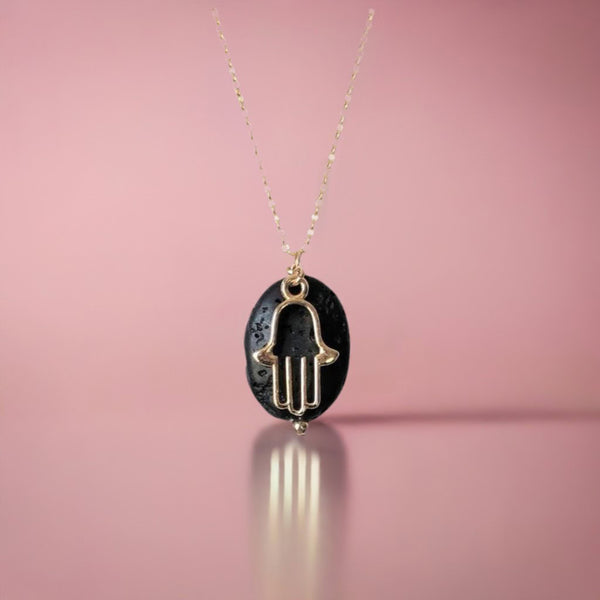 A hamsa aromatherapy necklace on a pink background
