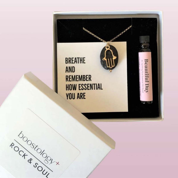 A hamsa diffuser necklace and bottle of essential oil in a white gift box