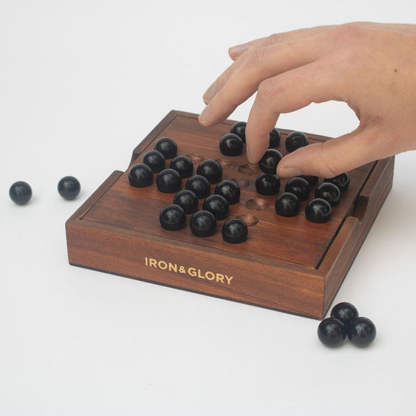 Someone playing with a glass marble on the wooden Solitaire set