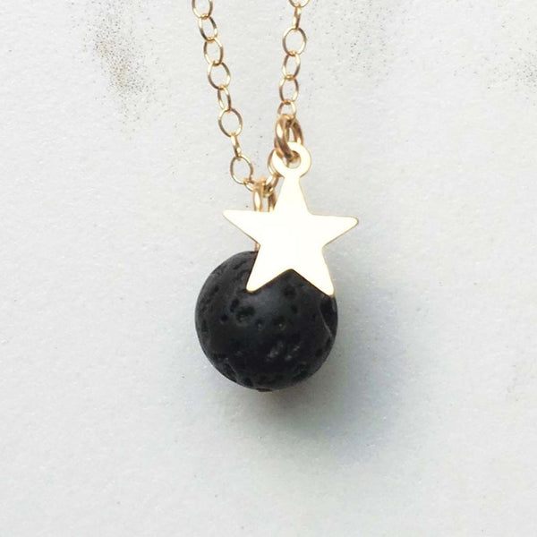 A close up of the gold star lava diffuser necklace on a white marble background
