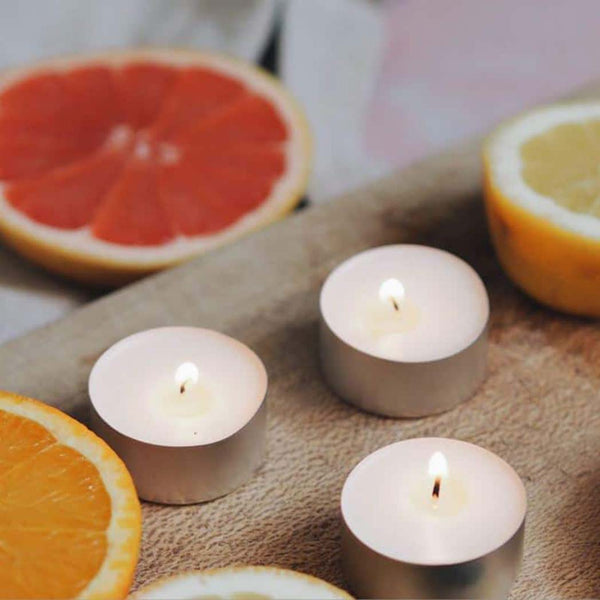 Three tea light candles alight, next to halved oranges