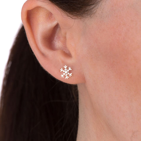 A silver snowflake stud earring in a woman's ear