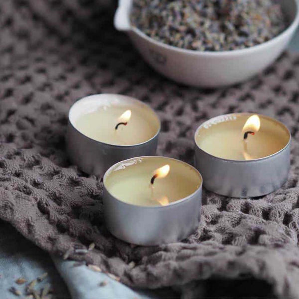 Three lit tea light candles next to a bowl of lavender