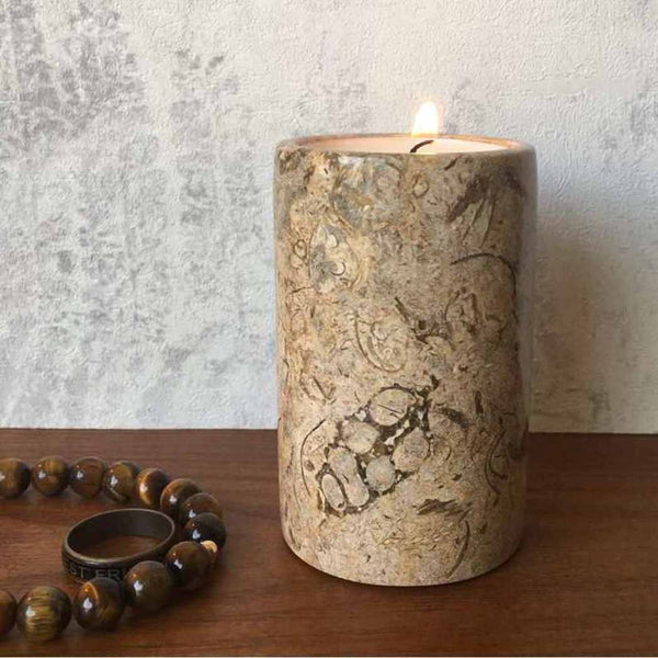 A fossil stone tea light candle holder sat on a wooden surface next to a brown beaded bracelet