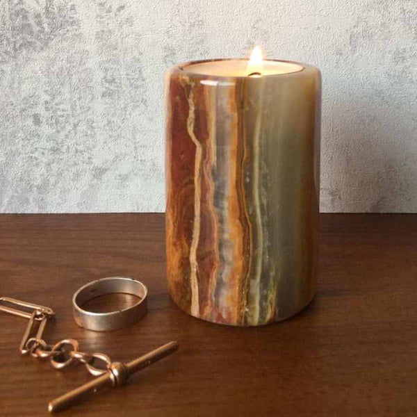 An Onyx stone tea light candle holder on a wooden surface sitting next to a necklace and ring
