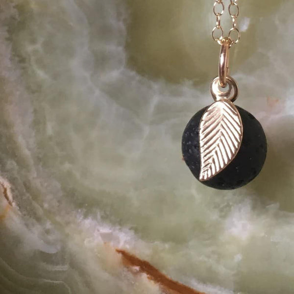 A gold leaf lava diffuser necklace on an Onyx stone background