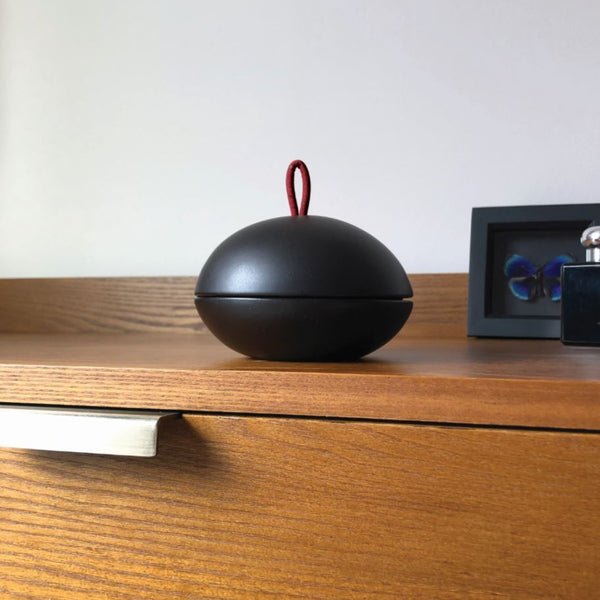 A black bonbonniere with a red cork leather handle on some bedroom drawers
