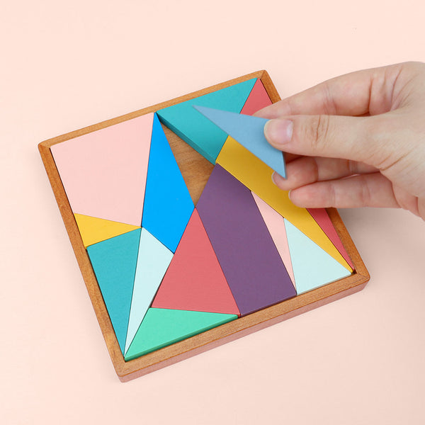 Colourful geometric puzzle with a hand placing a piece into the board, on a pink background