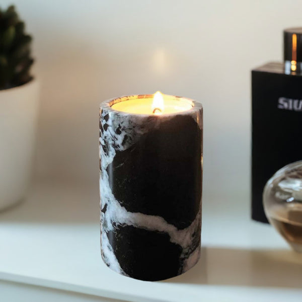 A black marble candle on a bathrrom shelf next to a fragrance bottle