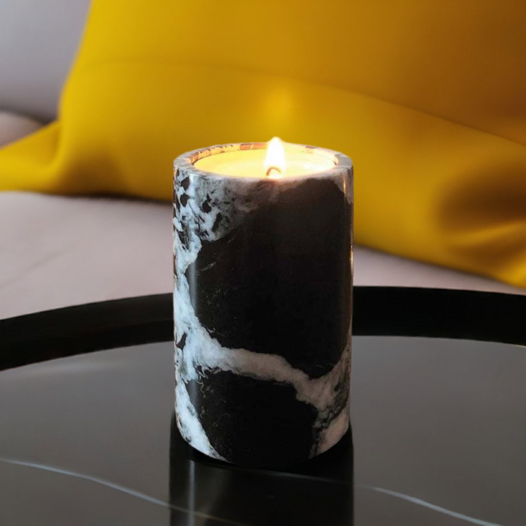 A black marble candle on a black coffee table with a bright yellow cushion in the background