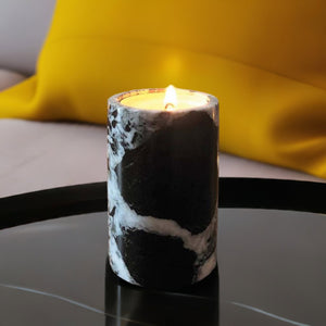 A black marble candle on a black coffee table with a bright yellow cushion in the background