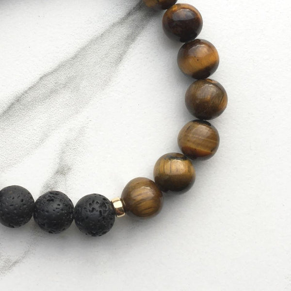 A tigers eye and lava stone diffuser bracelet on a white marble background