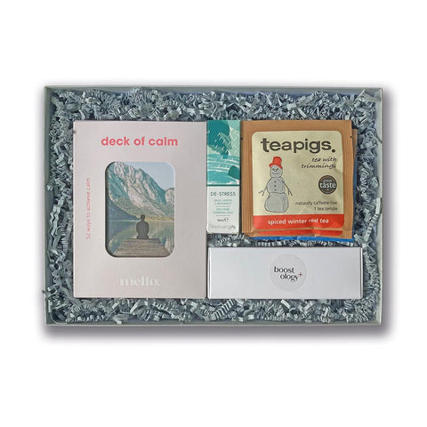 A silver grey Christmas hamper containing a deck of calm, essential oil, candles and Christmas teas, on a white background