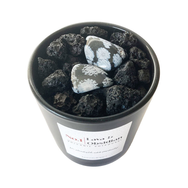 A black potpourri jar filled with black volcanic lava rocks and two black and white polished obsidian stones, featuring a white label on the front.