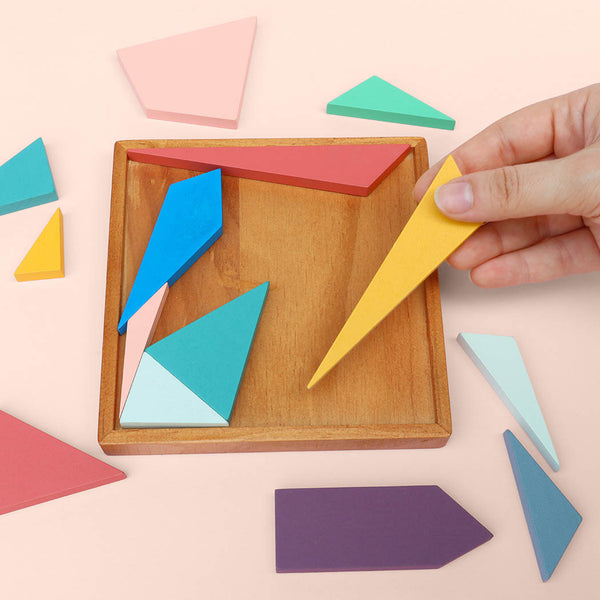 Colourful geometric shapes being placed into a wooden puzzle box, on a light pink background