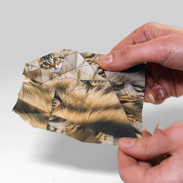 Hand holding a piece of origami paper with a cat's face on a plain background