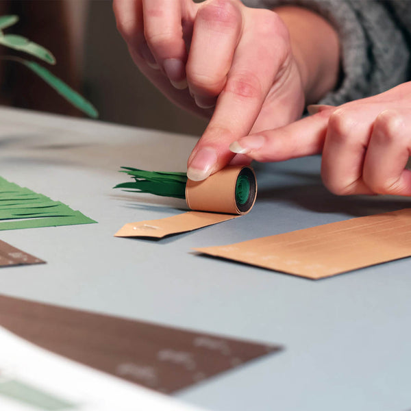 Person crafting a paper plant using strips of paper on a table