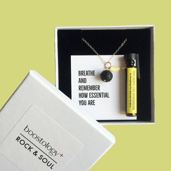 A lava diffuser necklace in a white gift box with the words "breathe and remember how essential you are"