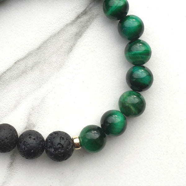 A green tigers eye and lava stone diffuser bracelet on a white marble background