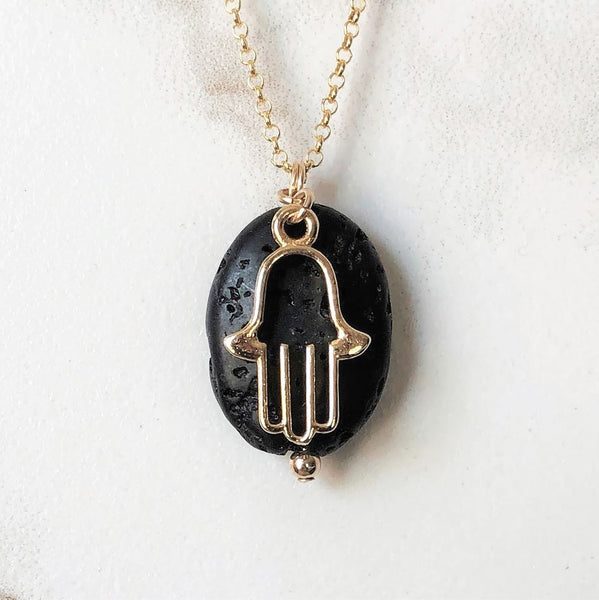 A gold hamsa charm and black lava bead on a gold chain