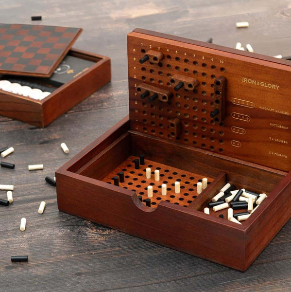 A wooden direct hit battleship game on a table with playing pieces scattered around