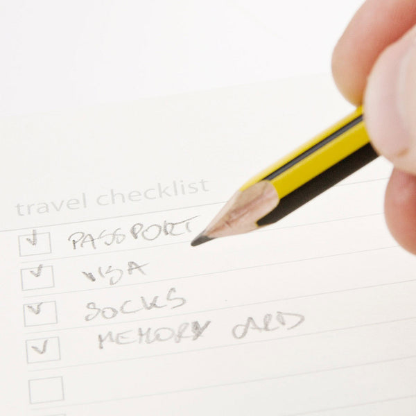 Hand holding a pencil over a travel checklist on a white background