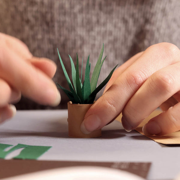 Close-up of hands holding a small paper plant with a blurry background