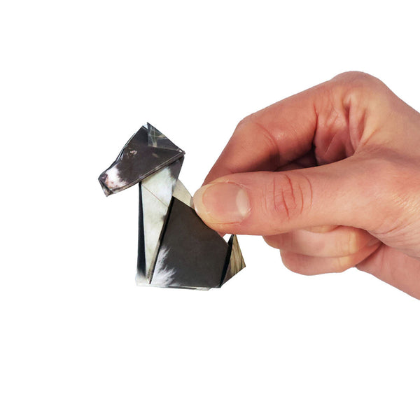 Hand holding a small, folded paper dog on a white background