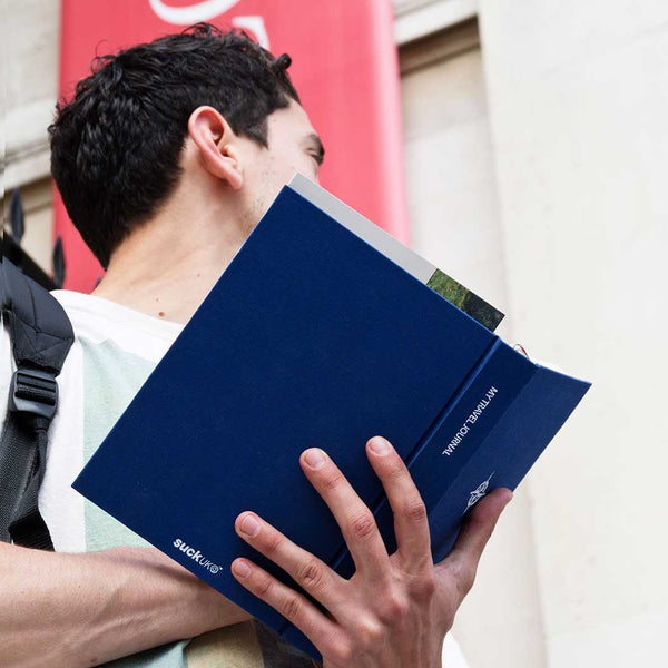 Person visiting a tourist attraction holding a blue travel notebook