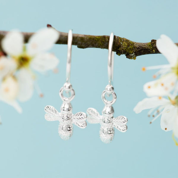 Two sterling silver bee drop earrings hanging from a blossoming branch