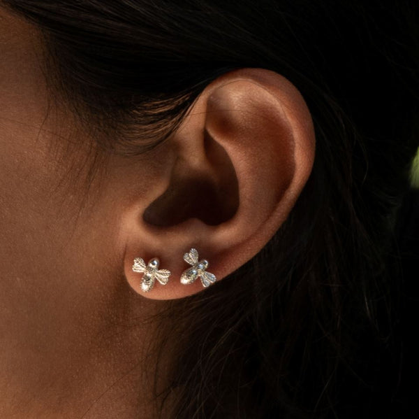 Two silver bee stud earrings in a woman's ear