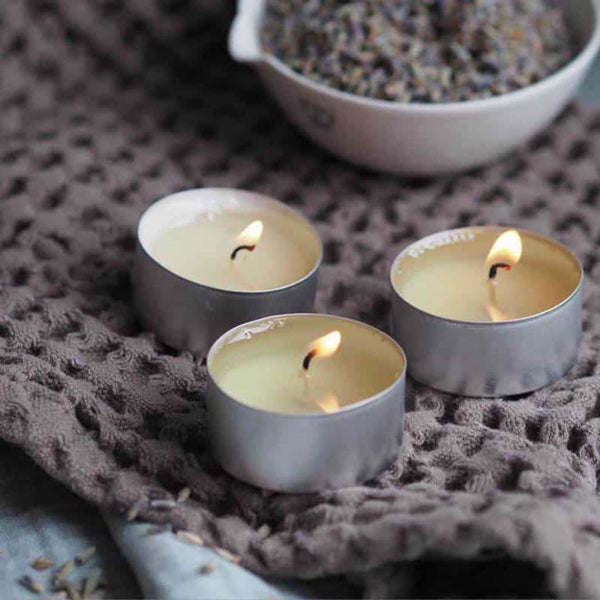 Three lit tea light candles next to a bowl of lavender flowers