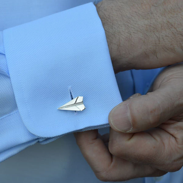 A Silver paper plane cufflink on a blue shirt sleeve 