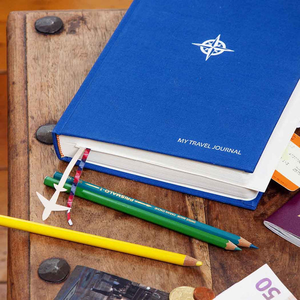 Blue travel journal with compass design on a wooden surface with pencils and coins.