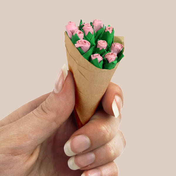 Hand holding a cone-shaped bouquet of pink flowers against a beige background