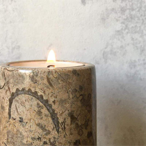 A fossil stone tea light candle holder with a lit candle