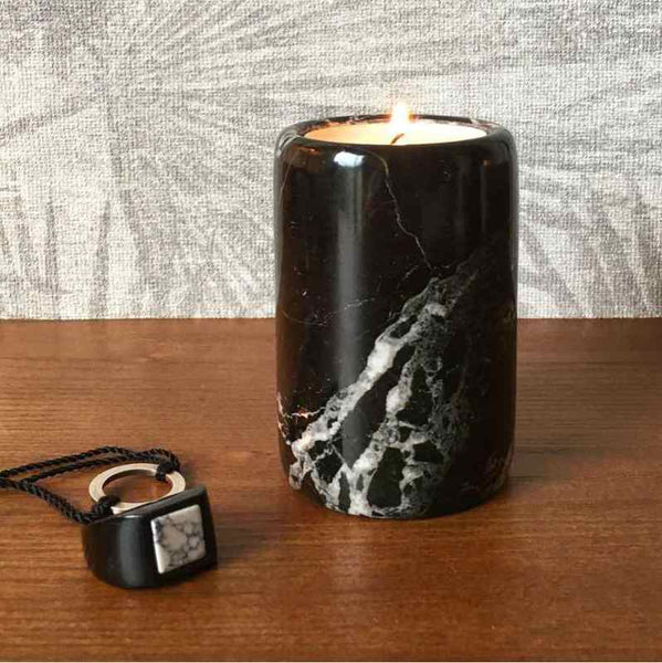 A black marble tea light candle holder on a wooden surface next to a ring and necklace